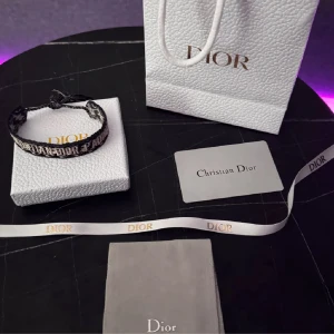 Dior armband - Snyggt armband från Dior i blått och beiget med broderad logga runt om. Armbandet är justerbart med knytning och har fransar i ändarna. Perfekt accessoar för att lyfta din outfit med en lyxig touch och streetkänsla.