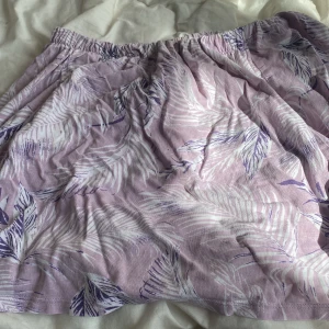 Ljuslila kortkjol med bladmönster H&M - Superfin ljuslila kortkjol från H&M med vitt och lila bladmönster. Kjolen har resår i midjan och är gjord i mjuk bomull, perfekt för varma dagar. Snygg och avslappnad passform som är lätt att styla med en enkel topp.