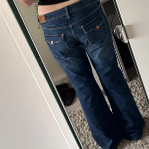 Blå bootcut jeans med låg midja - Säljer ett par mörkblå jeans med bootcut passform och låg midja. Jeansen har klassiska fickor med snygga kopparfärgade nitar och detaljerade sömmar. Perfekta för dig som gillar en avslappnad men ändå trendig look. Lite baggy. Fit star (H&M)