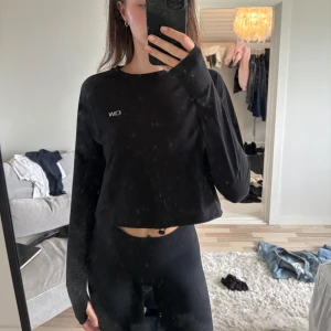 Svart träning croppad långärmad tröja - Svart långärmad croppad tröja från icaniwill med enkel design och liten vit logga på bröstet. Tröjan har en loose passform och är tillverkad i mjukt bomullsmaterial, perfekt till chill eller träning. Rund halsringning och stilren look.