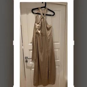 Klänning  - Snygg långklänning i satin-look från lovisa barkmans kollektion med BikBok. Halterneck modell med öppen rygg och långa knytband. Slits framtill. Aldrig använd, prislappar kvar! Storlek 44.