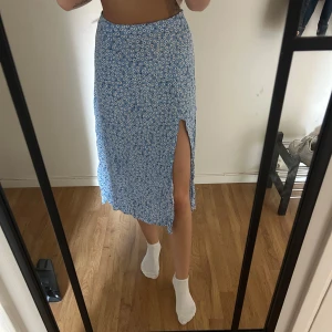 Blommig blå långkjol med slits - Säljer en blå långkjol med vita småblommor och en snygg hög slits på ena sidan. 