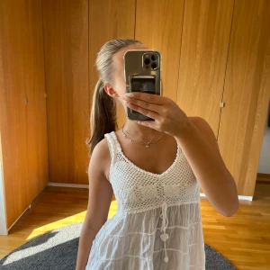 Vit somrig klänning med virkade detaljer - Superfin vit klänning med virkade detaljer upptill och knytband under bysten. Klänningen är ärmlös, har v-ringning och ett flowy fall. Perfekt för varma dagar och ger en riktigt fräsch och bohemisk vibe.