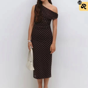 Brun prickig one shoulder klänning - Supersnygg svart långklänning med vita prickar och one shoulder-design. Klänningen har figurnära passform och ärmlös stil med asymmetrisk axel. Perfekt för dig som vill sticka ut med en trendig och elegant look.