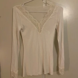 Vit långärmad topp från intimissmi - Supersöt vit långärmad topp med v-ringning och fina spetsdetaljer vid halsringningen och ärmsluten. Tunn och mjuk, perfekt att styla med jeans eller kjol för en romantisk vibe.