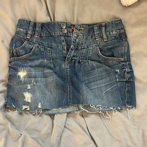 Blå jeanskjol med slitningar  - Snygg blå jeanskjol från QS med slitna detaljer och fransig nederkant. Perfekt för dig som gillar en edgy och avslappnad stil.