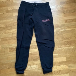 Svarta mjukisbyxor från Hoodrich S - Svarta mjukisbyxor från Hoodrich i storlek S. Byxorna har dragsko i midjan, ribbade muddar vid bensluten och HOODRICH-logga i rött och vitt på låret. Perfekta för chill eller streetwear. Mjukt material och fickor med dragkedja.