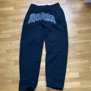 Svarta mjukisbyxor från Hoodrich S - Svarta mjukisbyxor från Hoodrich i storlek S. Byxorna har en bred resår i midjan med snörning och stor broderad Hoodrich-logga framtill. Tillverkade i mjukt bomullsmaterial för maximal komfort och avslappnad stil.