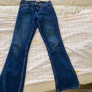 Blå bootcut jeans från Gina Tricot - Snygga blå jeans från Gina Tricot i klassisk bootcut-modell. Jeansen har normal passform och är tillverkade i ett mjukt denimtyg med lätt slitning. Perfekta för dig som gillar en retro vibe och vill ha ett par jeans som sticker ut lite extra.
