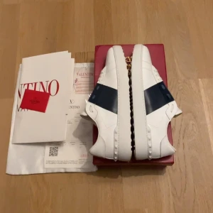 Valentino Garavani Open sneakers vit/blå - Snygga Valentino Garavani Open sneakers i vitt skinn med bred marinblå läderdetalj över mitten. Sparsamt använda. En defekt på lådan annars så gott som nya Tveka inte att höra av dig vid frågor eller funderingar. 