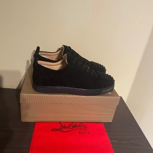 Svarta Louboutin sneakers med nitar - Snygga svarta sneakers från Christian Louboutin i mocka med svarta nitar på tån och klassisk röd sula. Skorna har snörning och en stilren, rund tå. Perfekta för dig som vill sticka ut med exklusiv streetstyle. Har använt de en gång till balen sedan har de bara legat på en hylla, har alla kvitton och så har jag dustbag. Om ni har frågor skicka ett dm svarar snabbt!