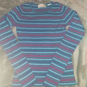 Randig ribbad tröja från JJXX XS - Använt denna en del men den är i väldigt bra skick. Säljer denna ribbade tröja från JJXX i storlek XS. Tröjan har ett färgstarkt randigt mönster i blått, lila och turkost. Den är figurnära och har rund halsringning. Materialet är en mix av viskos, nylon och polyester för en mjuk och stretchig känsla.