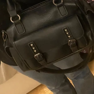Svart väska med nitar - Säljer denna svarta handväska💞jättelätt och styla, bra med utrymme och fack💞 använd ett fåtal gånger, vet tyvärr ej märket!