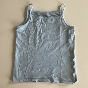 Ljusblå linnetopp från H&M - Säljer en ljusblå linnetopp från H&M med tunna axelband och söt spetskant upptill. Toppen är ärmlös och har en enkel, rak passform. Perfekt för varma dagar och enkel att matcha med jeans eller shorts.