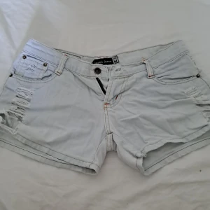 Ljus ljusblåa jeansshorts low waist - Jättefina jeansshorts som har en väldigt ljus nyans av blå. Med slitna detaljer och många detaljer på ena bakfickan. Köpt från en marknad i Thailand.