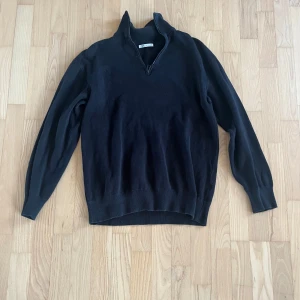 Svart stickad tröja med half zip från Zara - Svart stickad tröja från Zara med halv dragkedja i halsen. Tröjan har långärmade och ribbade muddar vid ärmslut och nederkant. Perfekt för dig som gillar enkel och stilren design med lite sportig touch. Passar dig som vill ha en klassisk look.
