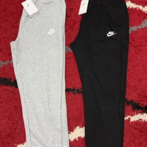 Nike mjukisbyxor svart & grå  - Två par mjukisbyxor från Nike, ena i ljusgrått och andra i svart. Båda har klassisk Nike-logga på låret och elastisk midja för skön passform. Perfekta för chill eller träning, tillverkade i mjukt bomullsmaterial. Snygg och enkel design som funkar till allt. 350 för en