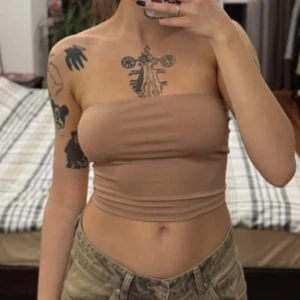 Beige bandeau tubtopp från Shein - Säljer en beige bandeau tubtopp från Shein i storlek XS. Toppen är ärmlös och croppad med en enkel, slät design och mjukt stretchigt material som sitter snyggt mot kroppen. Perfekt för dig som gillar minimalistisk stil och vill ha en basic topp till sommaren.