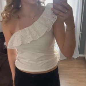 Vit oneshoulder topp med volang - Supersöt vit oneshoulder topp med volang i broderad spets. Ifrån Lindex storlek M!