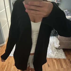 Svart  ribbad mellan  lång kofta - Säljer en svart, långärmad cardigan jacka med enkel och stilren design. Jackan är öppen framtill och har en loose passform som gör den skön att bära. Perfekt för dig som gillar en chill och avslappnad look. använd 1 gång