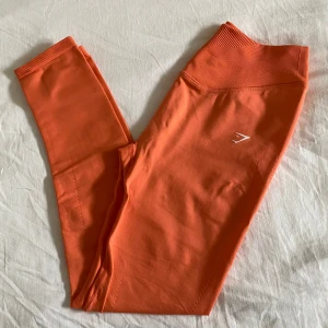 Sweat seamless leggings från Gymshark - Snygga oranga leggings från Gymshark med hög midja och ribbad linnin. Stretchigt material som sitter tight och följer kroppen, ventilerande håldetaljer på baksidan av benen. Superskön passform och cool färg. Använda endast en gång, nyskick! Slutsåld på hemsidan✨