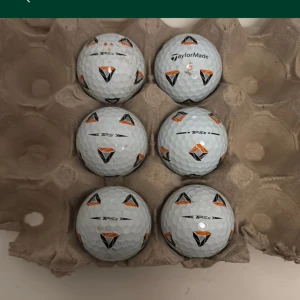 Golfbollar - Bilderna visar golfbollar av märket TaylorMade TP5 och TP5x, placerade i en äggkartong. Det finns ingen bok synlig på bilderna, endast sportutrustning för golf.