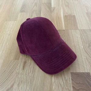 vinröd keps i manchester - Vinröd keps från NN07 i mjuk manchester med klassisk böjd skärm och justerbar rem bak. Nyskick.