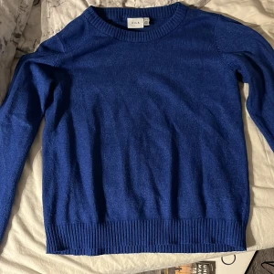 Blå stickad tröja från VILA - Snygg blå stickad tröja från VILA i storlek M. Tröjan har rund halsringning, ribbade muddar vid ärmslut och nederkant samt långärmad passform. Perfekt att matcha med jeans för en chill look. Materialet känns mjukt och skönt mot huden.