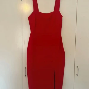 Röd långklänning med slits - Säljer en snygg röd långklänning med breda axelband och rak halsringning. Klänningen har en tight passform och en stilren slits framtill som ger en cool vibe. Perfekt för dig som vill sticka ut med en enkel men effektfull look.