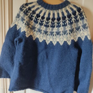 Blå stickad tjocktröja - Säljer en blå stickad tröja med ett vitt klassiskt mönster runt halsen. Materialet är stickat i ull och väldigt tjock så den är varm och perfekt för kalla vinterdagar. Garnet är lite skadat på ett ställe vid halsen, bild av det på den sista bilen.