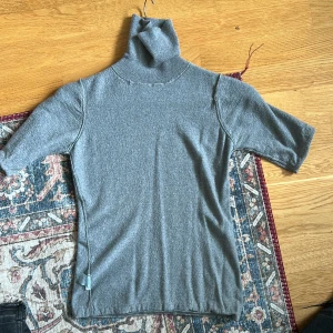 Grå polotröja - Säljer en enkel och stilren grå polotröja. Tröjan har korta ärmar och en hög polokrage som ger en chill vibe. Perfekt att matcha med jeans eller kjol för en clean look. Materialet är skönt och håller dig varm under kyliga dagar.