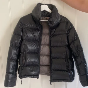Colmar jacka  - Snygg svart pufferjacka från Colmar med glansig finish och hög krage. Jackan har två sidofickor med dragkedja och ett stilrent Colmar-märke på ärmen. Fodret är grått och jackan stängs med dragkedja framtill. Storlek 38 men passar mig som har s/xs. Superbra skick. 