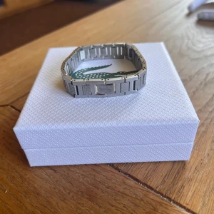 Silvrigt armband från Lacoste - Säljer mitt Lacoste armband i bra skick. Den är cirka 18cm lång och den går inte att göra större. Låda och påse till armbandet tillkommer vid köp. Kom privat för fler frågor 