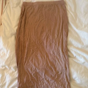 Beige långkjol i mjukt material - Säljer en beige långkjol med enkel och stilren design. Kjolen är figurnära och har en mjuk, stretchig känsla som gör den bekväm att bära. Passar perfekt till sneakers eller sandaler och är lätt att matcha med olika toppar.