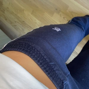 Mörkblå mjukisbyxor från BS, M - Mörkblå mjukisbyxor från BS med broderad logga på benet. Byxorna har elastisk midja och är tillverkade i mjukt bomull som är riktigt skönt mot huden. Passformen är utsvängd. Perfekta för chill eller träning.