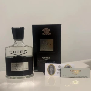 Creed Aventus Eau de Parfum 100ml - Creed Aventus är en lyxig parfym i en stilren glasflaska med svart och silverdetaljer. Flaskan rymmer 100 ml och har en svart kork. Förpackningen är svart med silverlogga och emblem. En ikonisk doft för dig som gillar exklusiva parfymer.