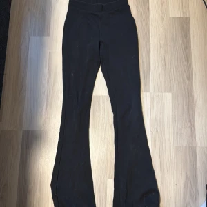 Svarta bootcut byxor i stretch - Svarta bootcut byxor i mjukt och stretchigt material, perfekta för dig som gillar en bekväm och snygg look. Byxorna har hög midja och sitter tajt upptill med utsvängda ben. Passar dig som är ca 14 år och vill ha en stilren vibe.