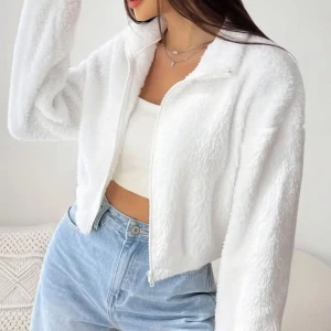 Vit croppad teddyjacka med dragkedja - Supermjuk och fluffig vit teddyjacka med croppad passform och dragkedja framtill. Jackan har lång ärm och en enkel, stilren design som är lätt att matcha med jeans eller kjol. Perfekt för dig som gillar en chill och cozy vibe.
