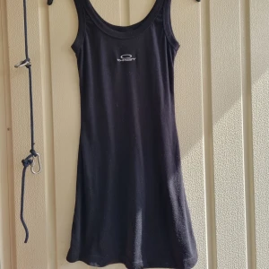 Svart långt linne från Okey - Snygg svart linne/klänning från Oakley med sportig look. Modellen har en slim passform som sitter skönt. Och den är lite nopprig. Skulle gissa på att den är storlek M/S
