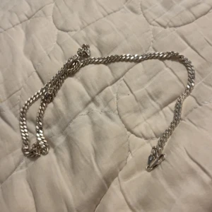 Kedjehalsband i silverfärg - Snyggt halsband med platt kedja i silverfärg. Låset är ett klassiskt karbinlås som gör det enkelt att ta av och på. Perfekt för dig som gillar stilrena accessoarer med lite edge. Passar både till t-shirt och hoodie.