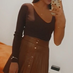 Mörkbrun ribbad långärmad topp - Snygg mörkbrun långärmad topp med ribbad struktur och djup v-ringning. Modellen är slim och sitter tajt mot kroppen, perfekt för att skapa en clean och stilren look. Materialet är mjukt och stretchigt, vilket gör den bekväm att bära hela dagen.