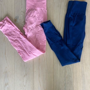 STRNGTH leggings rosa & marinblå - Två par leggings från STRNGTH, ett i ljusrosa och ett i marinblått. Båda har bred, ribbad hög midja med logga framtill. Stretchigt och mjukt material som sitter tight och följer kroppen, perfekt för gymmet eller chill. Snygg och enkel design utan mönster. Båda tightsen har scrunch som framhäver baksidan mycket bra!🩷💙storlek XS/S