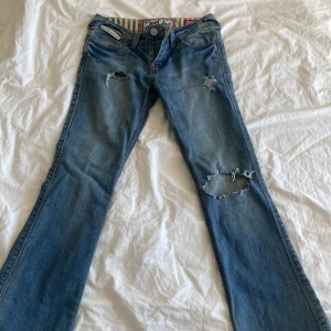 Blå bootcut jeans från Superdry - Säljer ett par blå jeans från Superdry i bootcut-modell med slitna detaljer och hål på båda benen. Jag köpte jeansen från vinted men dom var tyvärr för små💗 Midjemåttet är ungefär 39 cm, kolla på sista bilden. 