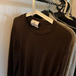 Brun merinoull tröja  - Snygg mörkbrun stickad tröja från The Factory med rund hals och långärmad passform. Tröjan är tillverkad i merinoull som känns skönt mot huden och har en klassisk, slim siluett. Perfekt för dig som gillar stilrena och enkla plagg.