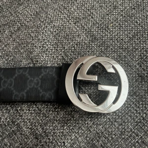Svart Gucci bälte med GG-spänne - Snyggt svart bälte från Gucci med klassiskt GG-mönster och stor, rund silverspänne med dubbla G. Bältet är gjort i äkta skinn och har en stilren look som lyfter vilken outfit som helst. Kommer med originalpåse och kort.