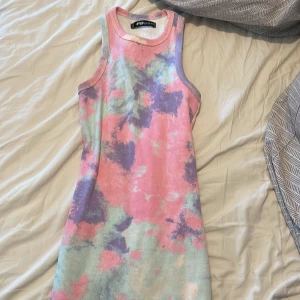 Pastellfärgad ribbad klänning FB Sister - Superfin kort ribbad klänning från New Yorker i storlek XS. Klänningen har ett färgglatt batikmönster i rosa, lila och ljusblått. Ärmlös modell med rund halsringning, perfekt för varma dagar och en chill vibe.