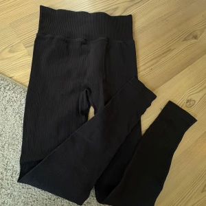Svarta ribbade träningsbyxor med hög midja - Svarta träningsbyxor med ribbad struktur och hög midja som sitter skönt och formar. Stretchigt material som passar perfekt till både chill och träning. Snygg, enkel design utan synliga loggor eller detaljer.