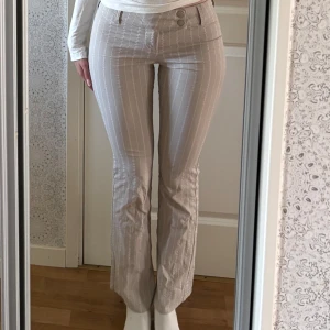 Bootcut kostymbyxor - Snygga beige/gråa kostymbyxor med vita vertikala ränder och bootcut-snitt. Byxorna uppfattar jag som lowrise. Säljer då byxorna är alldeles för korta för mig som är 172. Svårt att säga exakt vilken längd som passar men skulle gissa runt 160-165? 