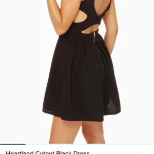 Svart cutout kortklänning - Supersnygg svart kortklänning med markerad midja, utställd kjol och coola cutout-detaljer i ryggen. Klänningen har breda axelband, dragkedja bak och ribbad struktur i tyget. Perfekt för dig som vill sticka ut med en modern och edgy look.