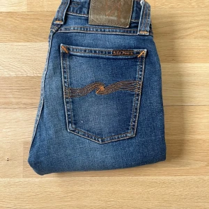 Nudie jeans slim fit  - Snygga blå jeans från Nudie Jeans med klassisk orange söm på bakfickan och läderpatch i midjan. Modellen är slim fit med normal midja och tillverkad i mjukt jeanstyg. Perfekta för dig som gillar en smal siluett och stilren look. Storlek 25/30 låter litet men de är ganska stora i storlek så jag som är 176 kan använda dom.
